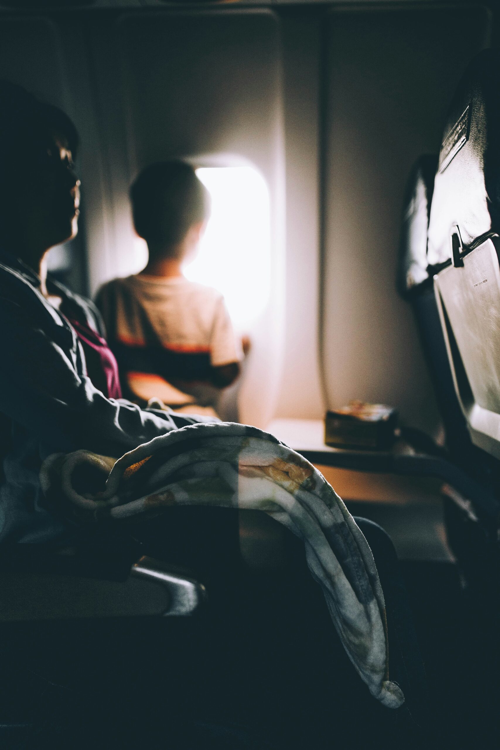 A woman and child seated on an airplane, looking out the window during a flight.