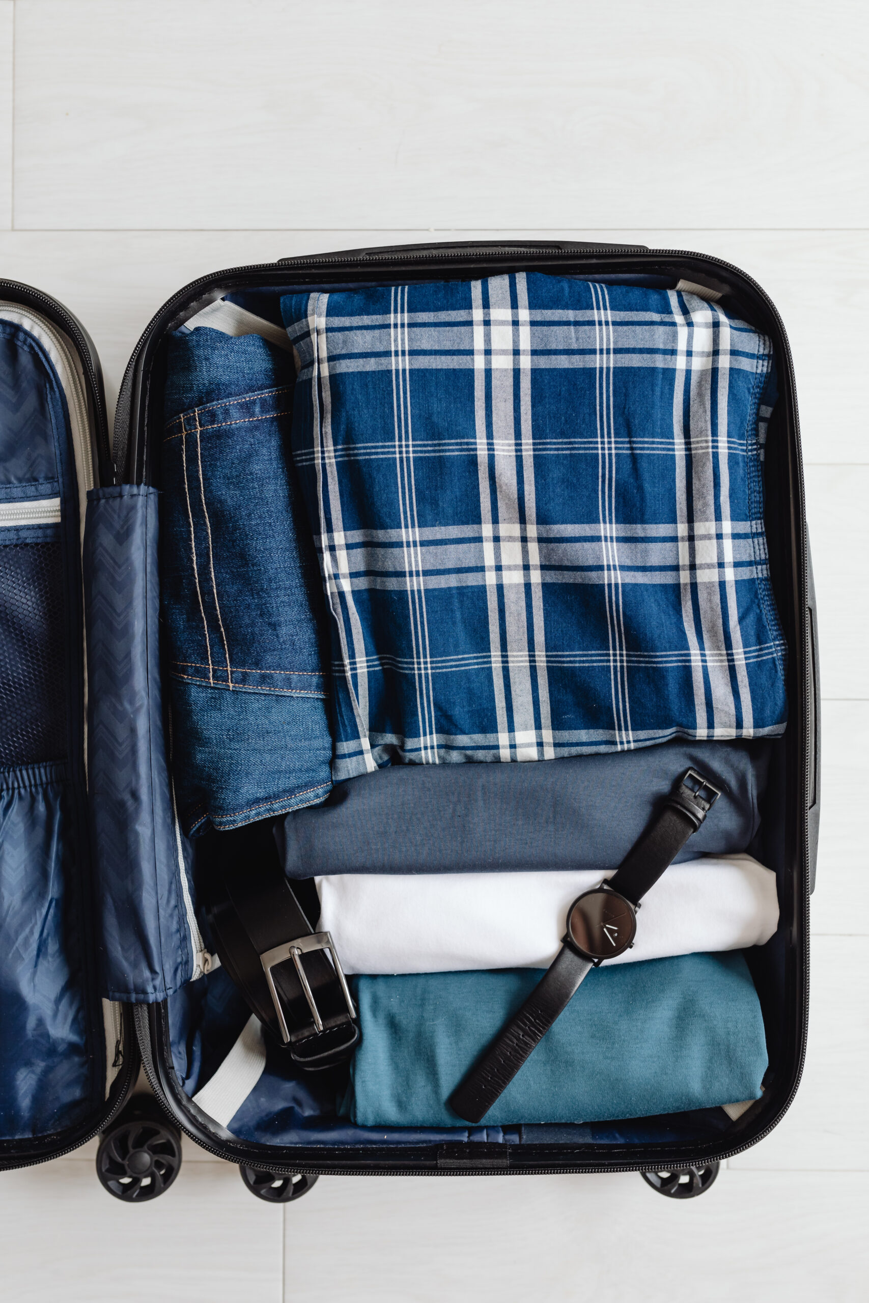 Open suitcase with folded clothes, a watch, and a belt, ready for travel.