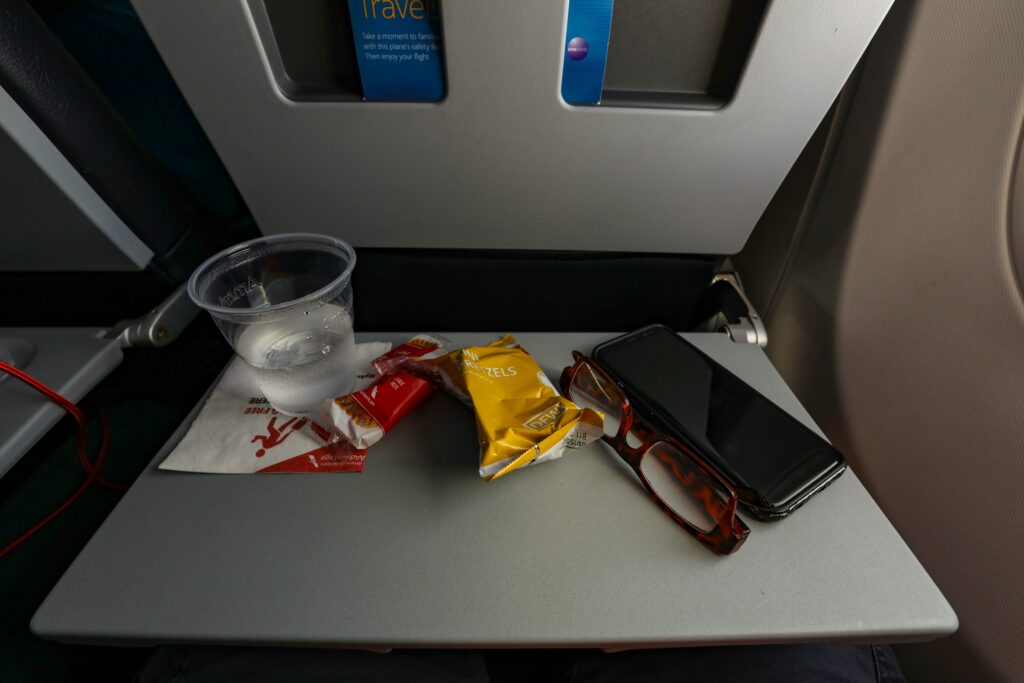 A tray table with water, snacks, phone, and glasses during an airplane flight.