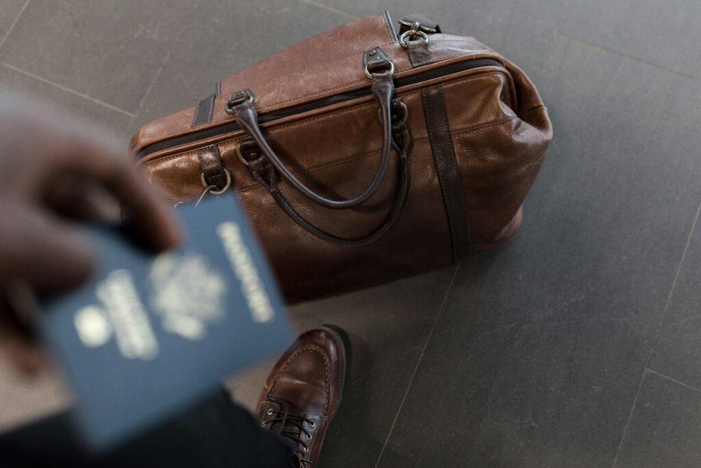 Leather duffel bag on floor with a hand holding a U.S. passport.