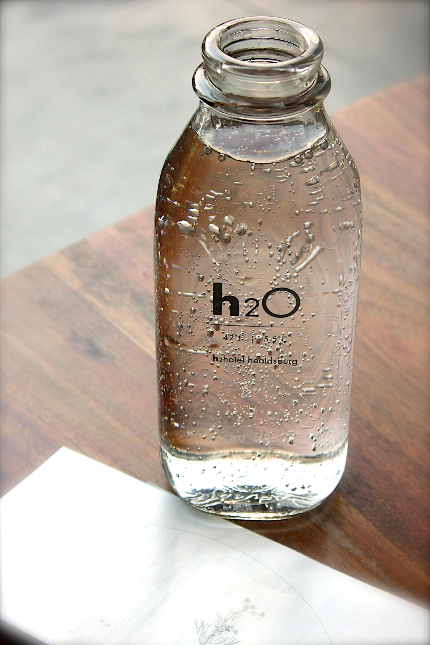 A clear glass water bottle labeled H2O on a wooden table.