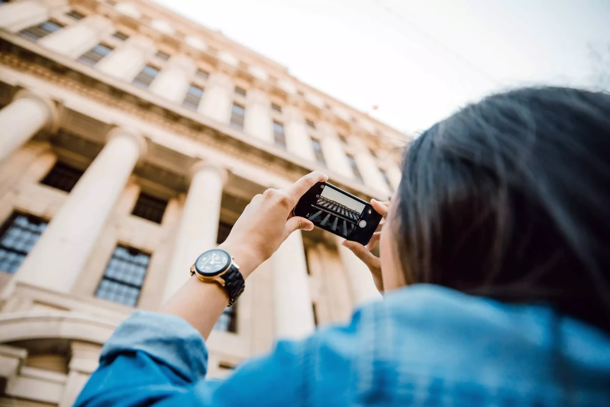 Tourist taking a photo of a neoclassical building with columns using a smartphone